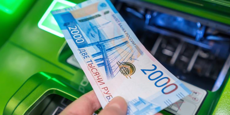Man's hand holds a new Russian banknote of two thousand rubles against the background of green cash machine.